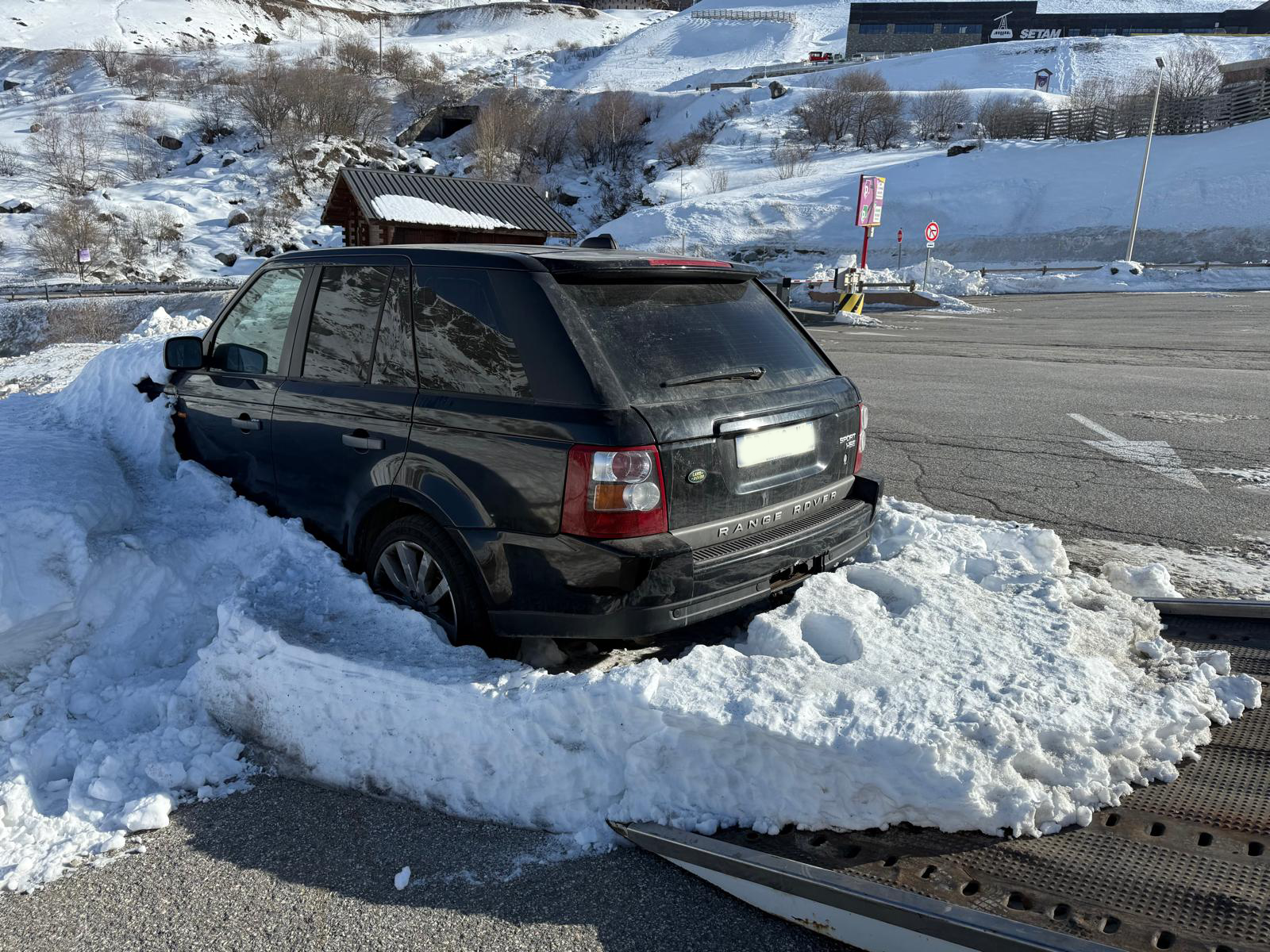 SUV noir embourbé dans la neige sur un parking de station de ski en montagne
